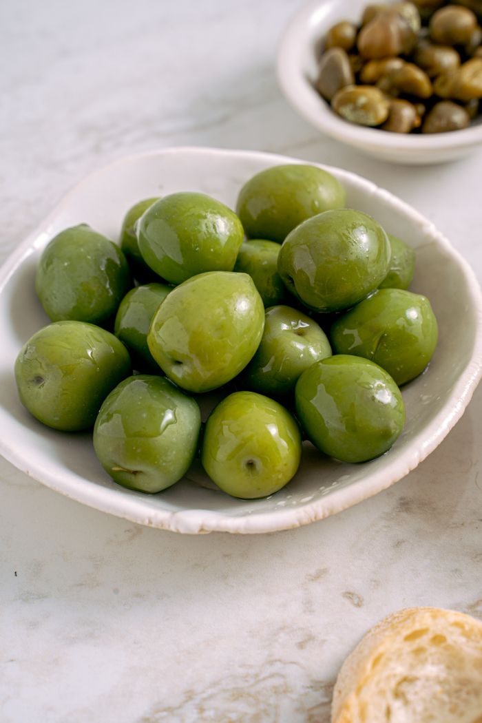 A close-up view of fresh green olives in a ceramic bowl on marble surface.